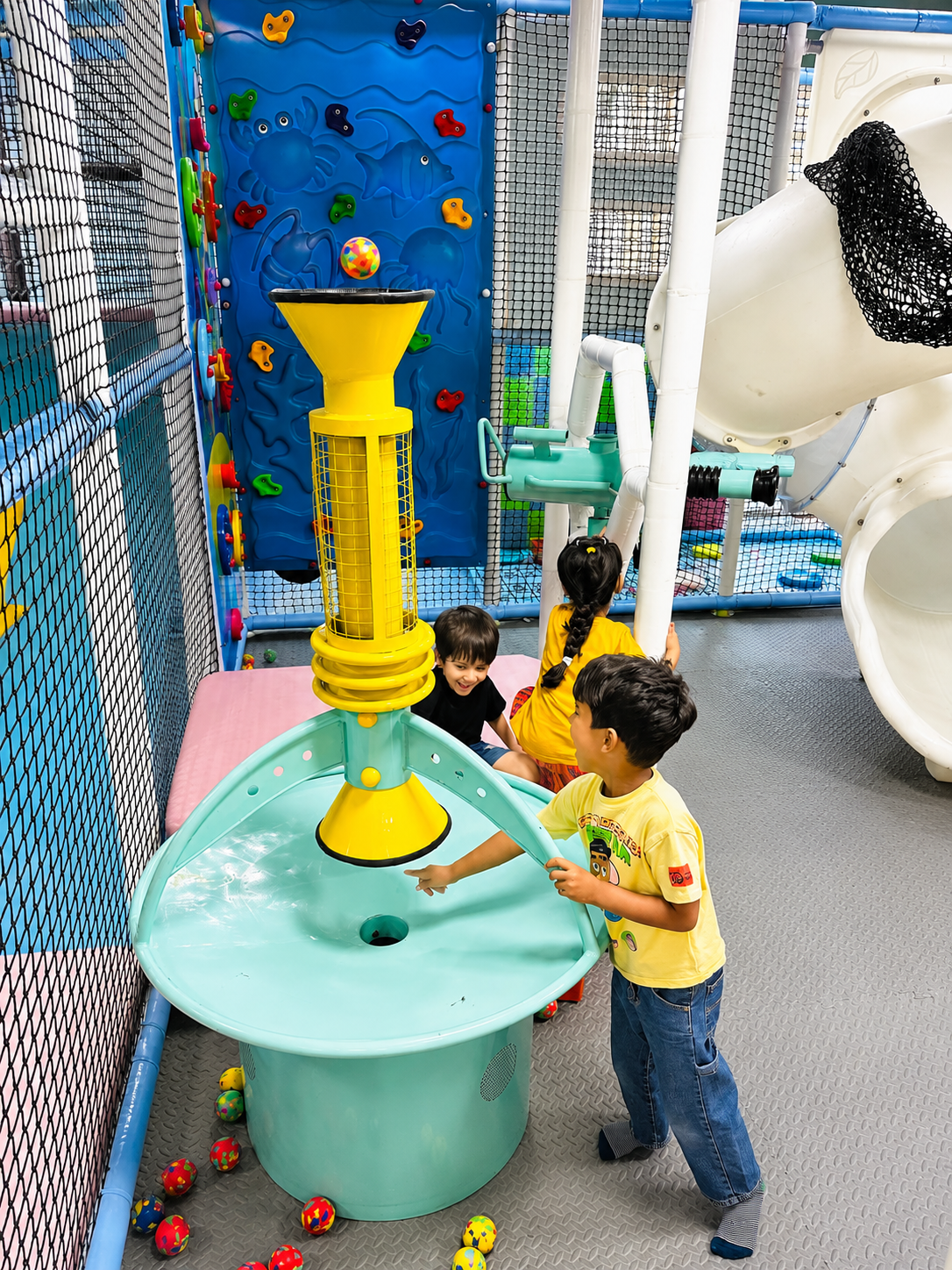 Kids playing at a ball-launcher soft play structure with climbing wall